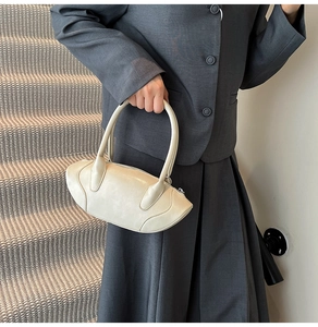 Minimalist beige matte leather handbag shown on model with tailored grey suit and steps