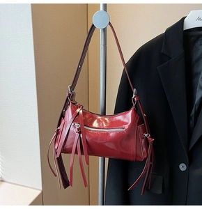 Detalle de bolso bandolera rojo oscuro con flecos largos y cremallera metálica decorativa