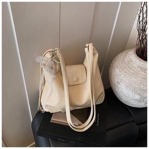 Detalle del bolso tote beige con textura de lichi y un colgante de lazo con encaje y perlas