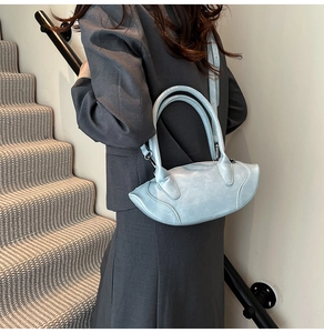 Light blue arc-shaped handbag with adjustable strap shown on a model in a gray suit