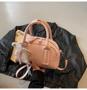 Close-up of pink leather Boston bag with pearl lace bow charm and crossbody strap