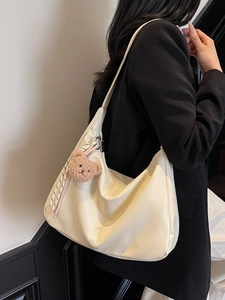 Elegant off-white faux leather hobo bag with teddy bear charm and wide shoulder strap