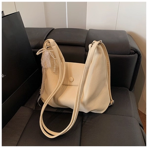Detalle de bolso tote beige con textura de grano y colgante de lazo de encaje de perlas