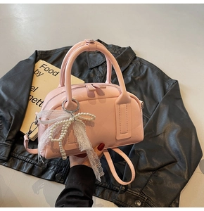 Close-up of pink Boston bag with elegant white lace bow and pearl charm details