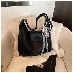 Detalle de bolso tote de cuero negro con dije de perlas y lazo de encaje en sofá