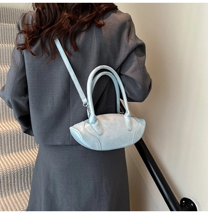 Close-up of light blue olive-shaped handbag with matte texture on model in grey suit