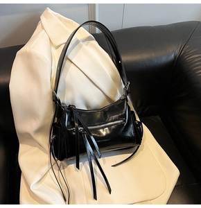 Detalle de bolso negro brillante con cremalleras plateadas y flecos largos en un blazer