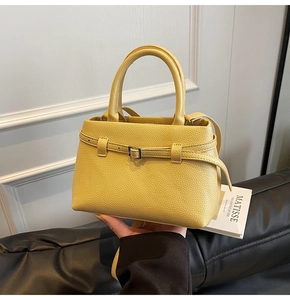 Detail of yellow lychee grain leather handbag with circular handles and metal buckles