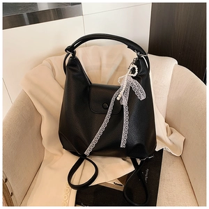 Detalle de bolso tote de cuero negro con lazo de encaje y colgante de perla sobre una americana
