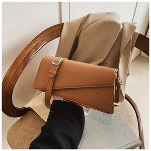 Detail of caramel leather clutch with asymmetric flap and slim strap in lifestyle setting