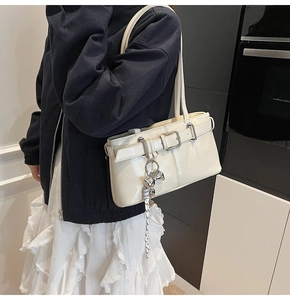 Dettaglio di una borsa a spalla color crema con fibbie argentate e ciondolo a fiocco