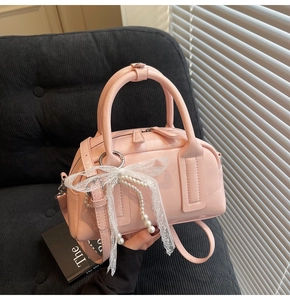 Pink Boston bag with white lace bow and pearl charms held against a cozy gray sofa