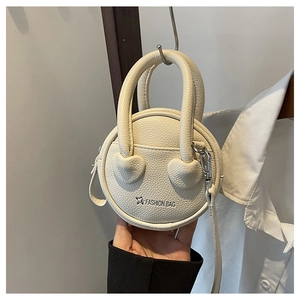 Détail d'un mini sac à main rond crème avec texture litchi et poignée en forme de cœur