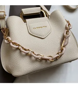 Detail of cream lychee leather bucket bag with gold semi-circle handle and resin chain