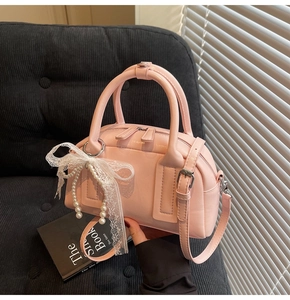 Close-up of pink Boston bag with pearl strap and lace bow on a corduroy sofa