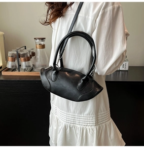 Detail of a matte black crescent handbag with silver hardware shown on a model