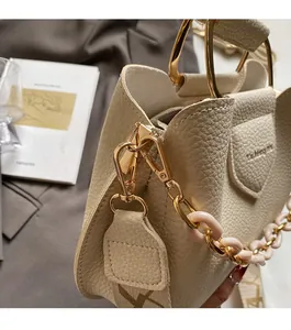 Detailed view of cream leather bucket bag with gold hardware and pink resin chain