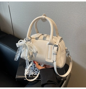 Detail of cream Boston handbag featuring pearl lace bow charm and adjustable strap