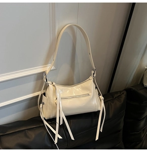 Detalle de bolso crema brillante con cremallera de borla y bolsillo lateral en el sofá