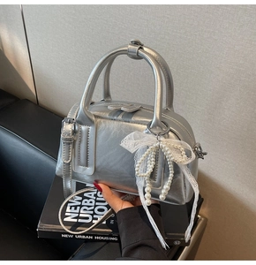Detail of silver metallic handbag featuring side pearl accents and delicate lace bow detail