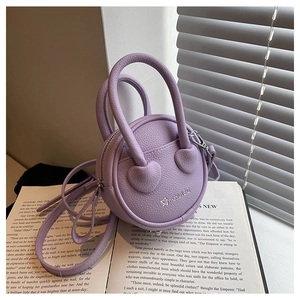 Détail du sac rond violet en cuir avec attaches cœur sur un livre ouvert au soleil