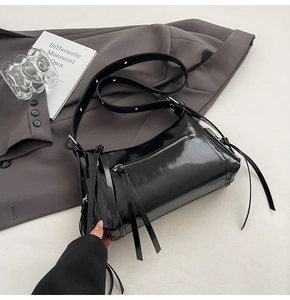 Detalle de bolso bandolera negro brillante con cremalleras y detalles de borlas