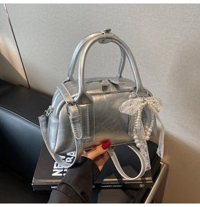 Detail of silver metallic Boston bag featuring pearl lace bow charm and premium hardware