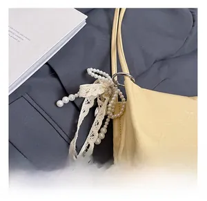 Détail d'un sac plissé crème avec un élégant accessoire de perles et de ruban de dentelle