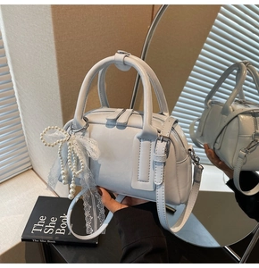 Detail of light blue Boston bag with pearl lace charm and glossy leather texture