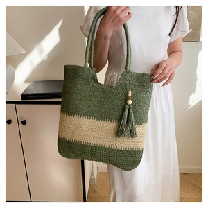 Detail of straw woven tote bag featuring olive green stripes and beaded tassel charm
