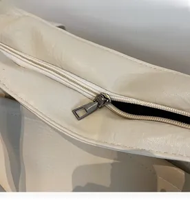 Detailed macro view of the smooth metal zipper and textured cream faux leather surface
