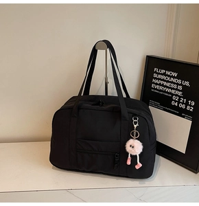 Detailed view of black travel bag with pink plush keychain and smooth zipper pocket