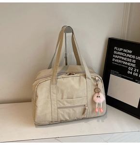 Close-up of the beige canvas travel bag featuring a front zipper pocket and plush ball charm