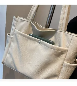 Detail of a minimalist beige tote bag showing its functional front snap pocket and pebble leather