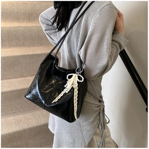 Détail d'un sac cabas plissé noir brillant orné d'un pendentif en dentelle et perles