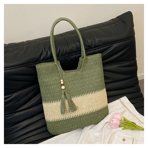 Close-up of a woven straw tote bag with green and cream stripes and decorative tassel