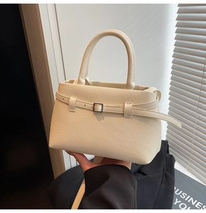 Detail of minimalist cream leather handbag with pebble texture and metallic buckle strap