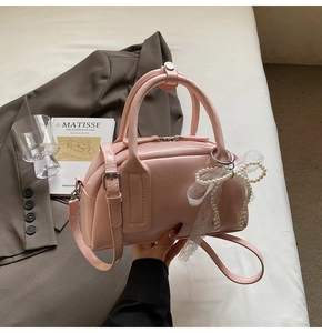 Pink leather Boston bag with elegant pearl bow charm on a soft lifestyle background