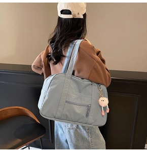 Close-up of light blue canvas travel tote with front zipper pocket and plush pendant