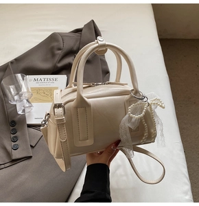 Detail of beige faux leather Boston bag featuring a pearl lace bow charm on the side