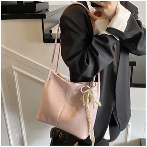 Détail du sac seau en cuir verni rose avec breloque nœud en dentelle et perles