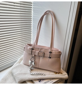 Dettaglio della borsa a spalla rosa chiaro con finitura lucida e ciondolo a fiocco su tessuto