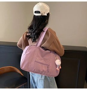 Rear view of model wearing a large purple travel tote with a soft decorative pompom charm