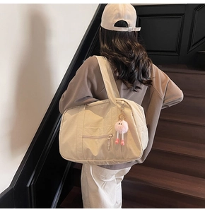 Detailed back view of a beige canvas travel bag with a pink plush doll charm