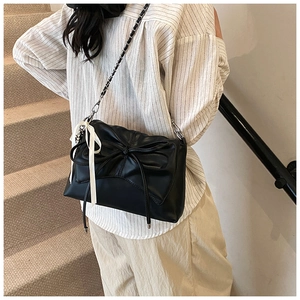 Detail of black bow shoulder bag featuring a silver chain strap and ribbon charm