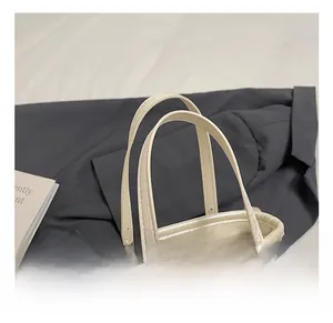 Detail of cream minimalist bucket bag showing round top handles and gold zipper hardware