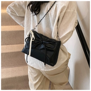 Detail of black bow shoulder bag with silver chain strap and white silk ribbon accent