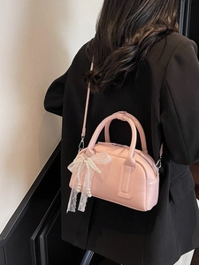 Pink Boston handbag with lace bow charm shown on model in a stylish indoor setting