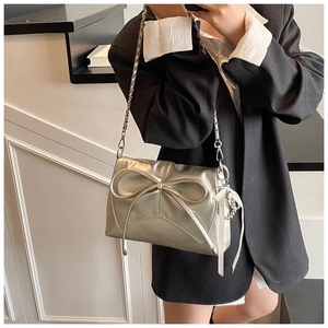 Detail of silver metallic crossbody bag featuring a large bow and thin chain strap