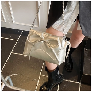 Silver bow shoulder bag with metal chain strap worn by model in minimalist setting